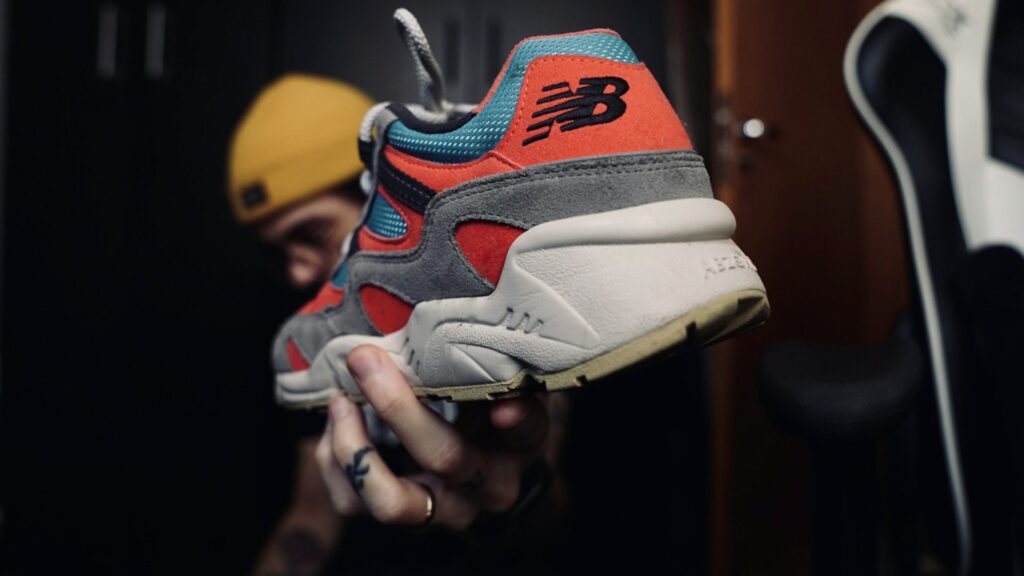 Hand toont sportieve New Balance sneaker in rood, blauw en grijs