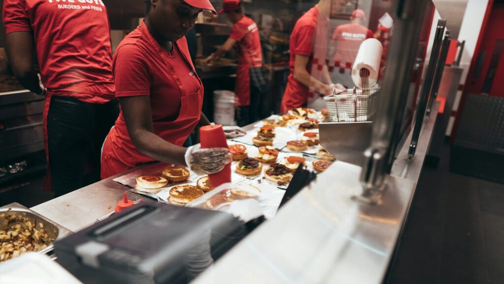 Medewerkers in een fastfoodketen bereiden hamburgers in een open keuken met zicht op de productielijn.