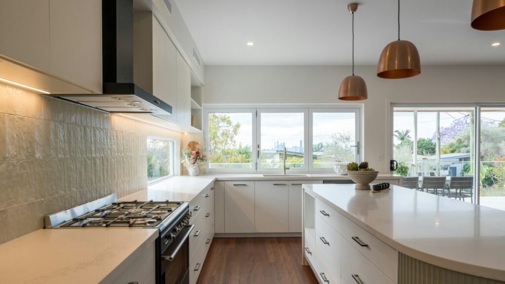 Lichte, moderne keuken met kookeiland, witte kasten en grote ramen – voorbeeld van stijlvolle binnenrenovaties.