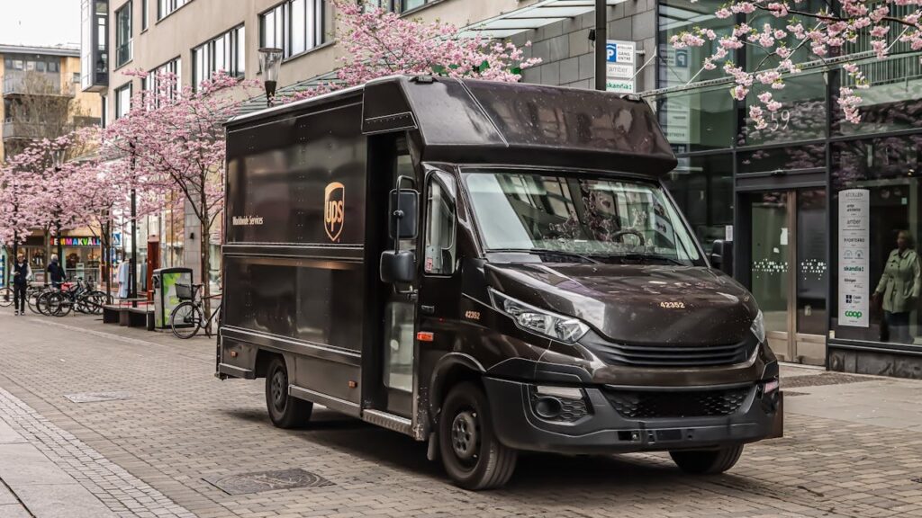 UPS-bezorgbus geparkeerd in een stadsstraat met bloeiende bomen, grootste pakketdiensten.