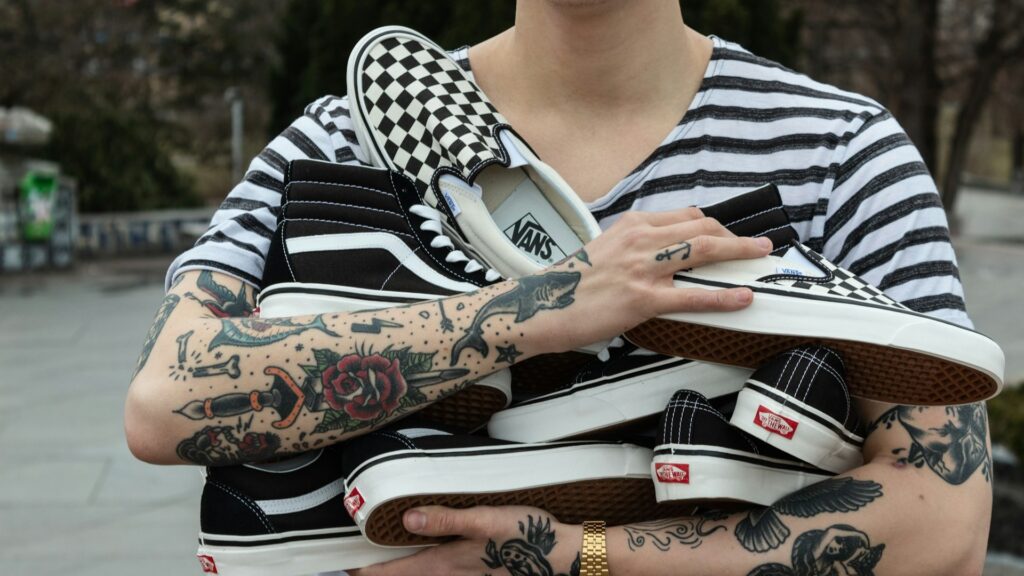 Getatoeëerde armen houden meerdere Vans schoenen vast, met checkerboard en zwart-wit design