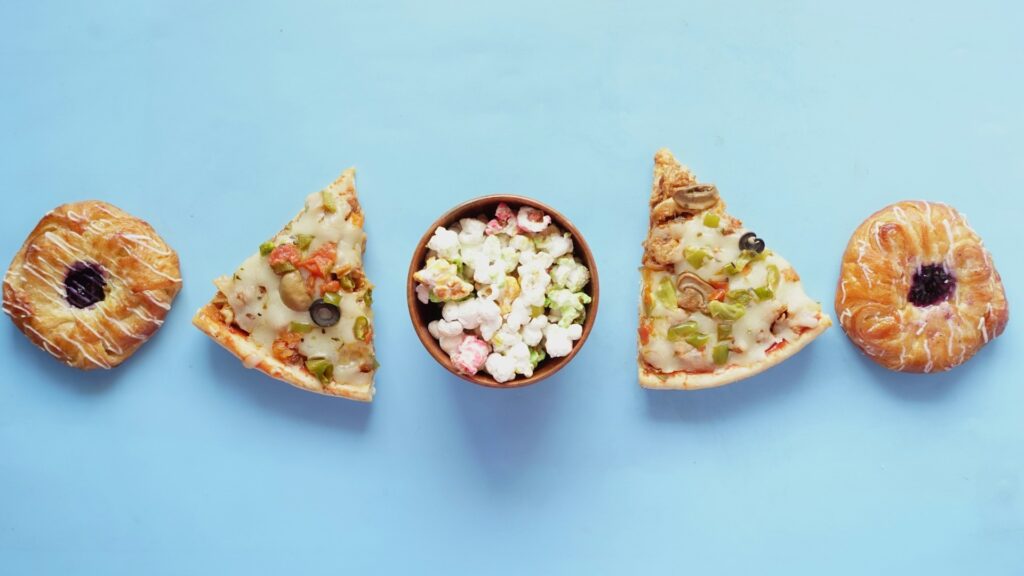 Voedingshypes met kleurrijke popcorn, pizza met groenten en zoete gebakjes op een blauwe achtergrond