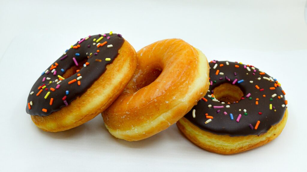 Drie donuts van een fastfoodketen, met chocoladeglazuur en gekleurde sprinkles op een witte ondergrond.